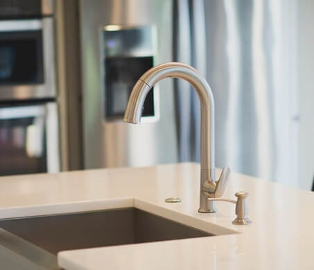 Chrome faucet and farmhouse style sink on island with solid surface countertop