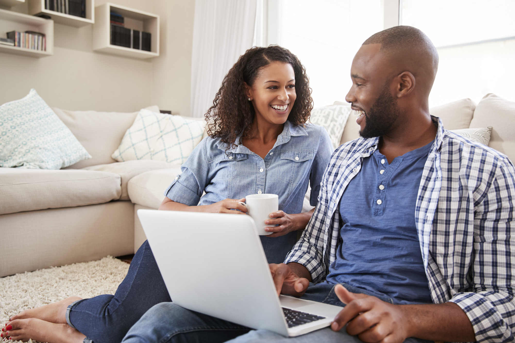Young black couple using laptop at home look at each other