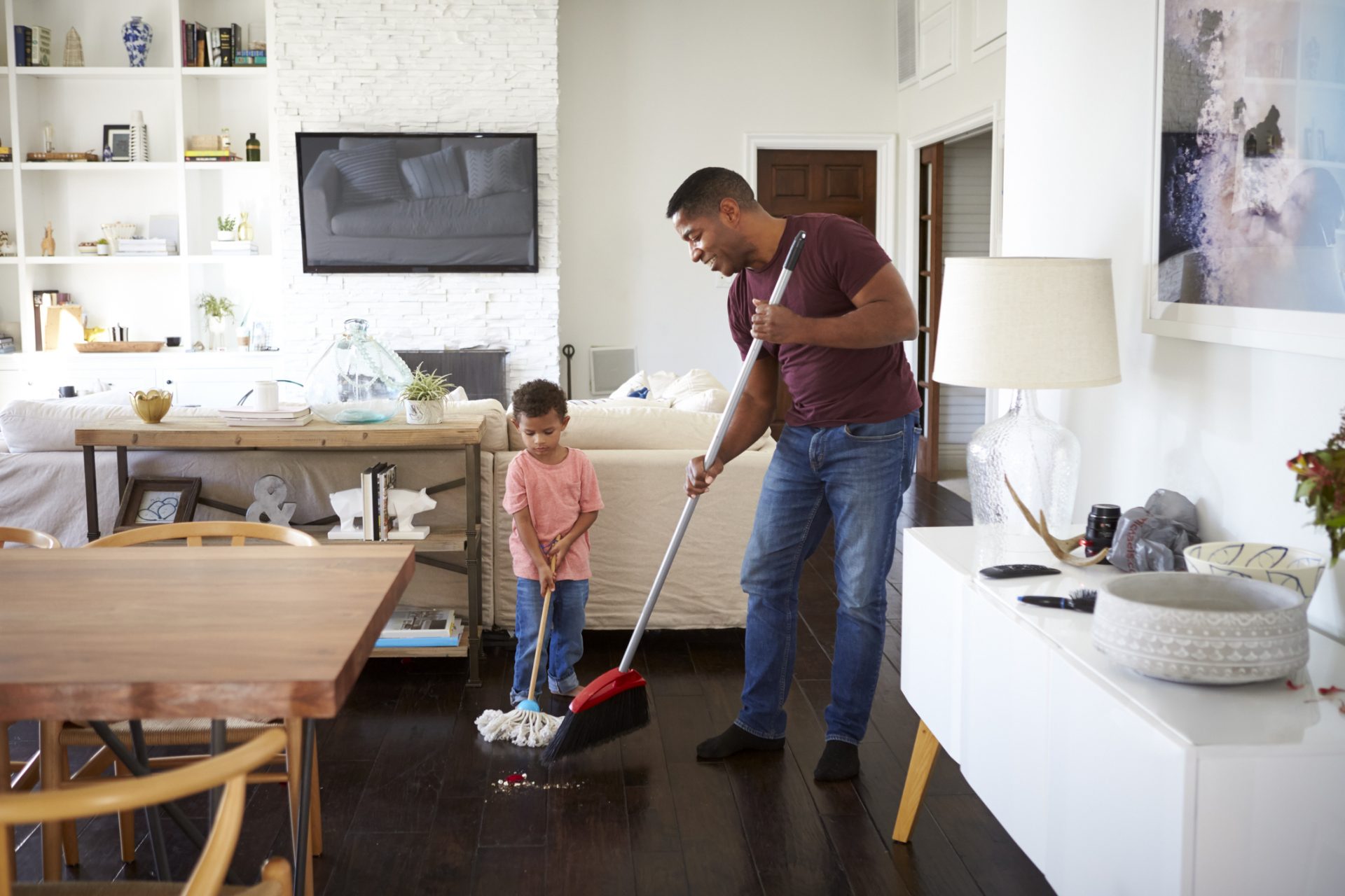 Grandfather and his three year old grandson mopping and sweeping the dining room floor, full length