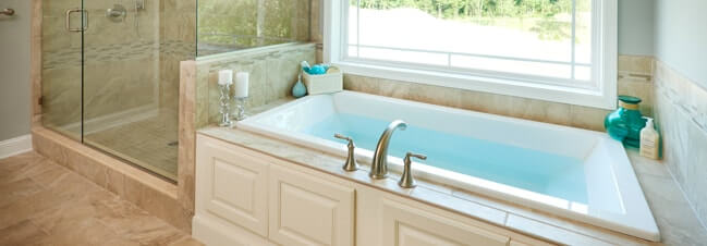 Soaking tub filled with water - large window above, and shower with glass door to the left