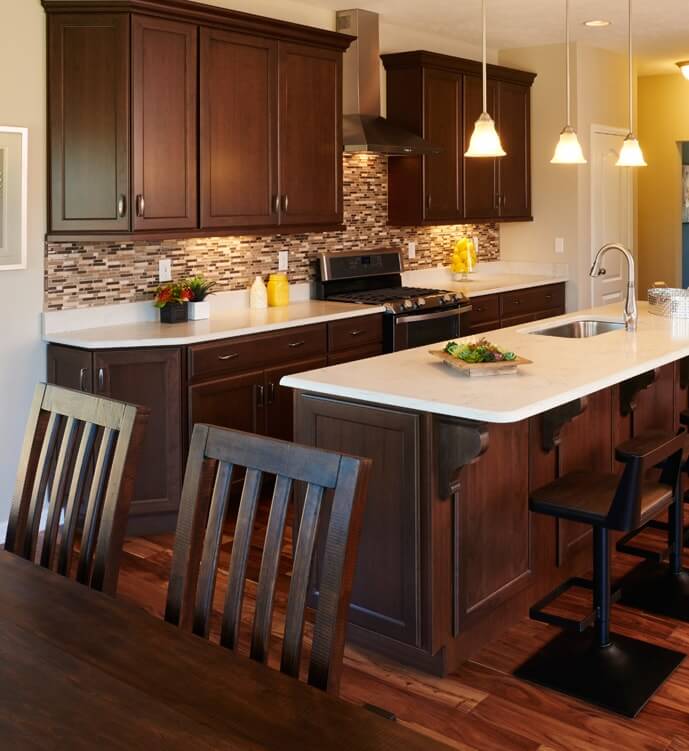 Kitchen with dark cabinetry, quartz countertops, tile backsplash, and large center island with sink and pendants above
