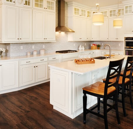 Kitchen with white cabinetry with glass panels along the ceiling, quartz countertops, and large center island with sink and overhang