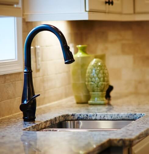 Brushed nickel faucet in kitchen with stainless steel undermount sink, granite countertops, and ceramic tile backsplash