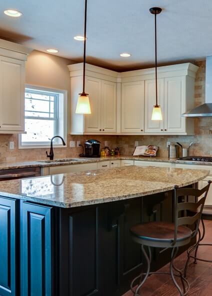 Kitchen with white cabinetry, large center island with granite countertops and bar overhang