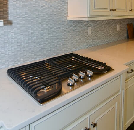Whirlpool stainless steel cooktop with black grates - set on granite counterops with white cabinetry