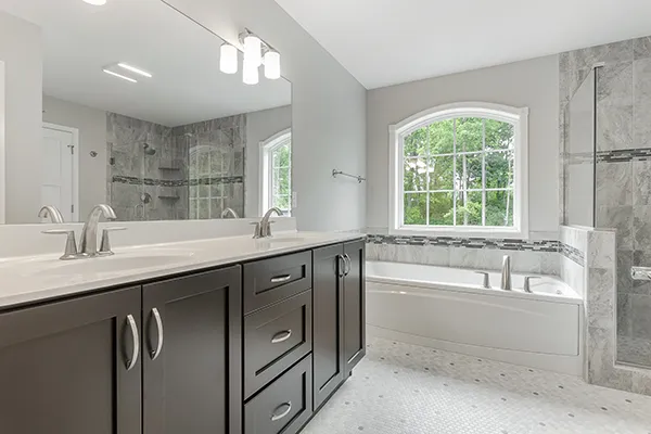 Avalon owner’s bathroom with dual vanity, soaking tub, tiled shower surround, and large window for natural light.