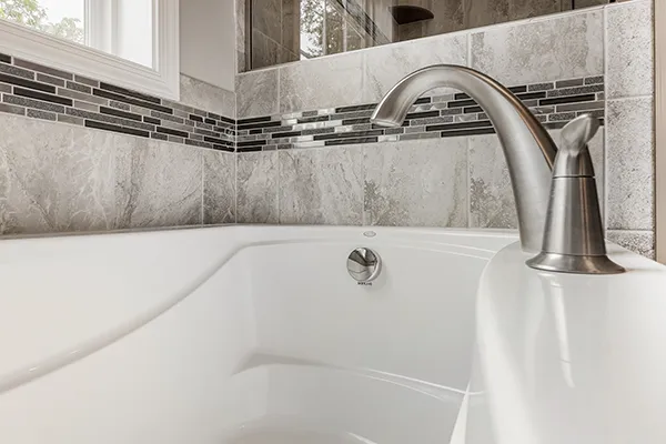 Deep soaking tub with brushed nickel faucet, ceramic tile surround, and decorative accent tile.