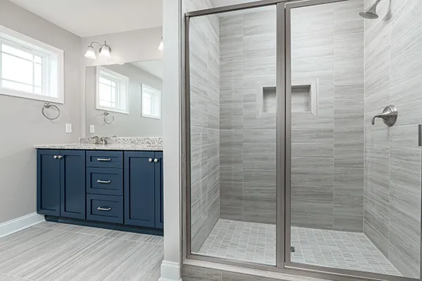Crestmont luxury owner’s bath with dual vanities, blue cabinetry, granite counters, and ceramic tile shower.