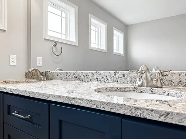 Close-up of quartz vanity countertop with undermount sink, brushed nickel faucet, and backsplash detail.