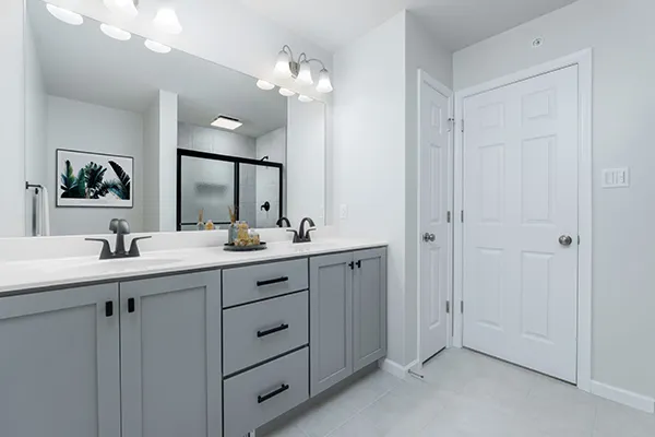 Woodfield luxury owner’s bath with dual vanity, gray cabinetry, oversized mirror, and tiled shower