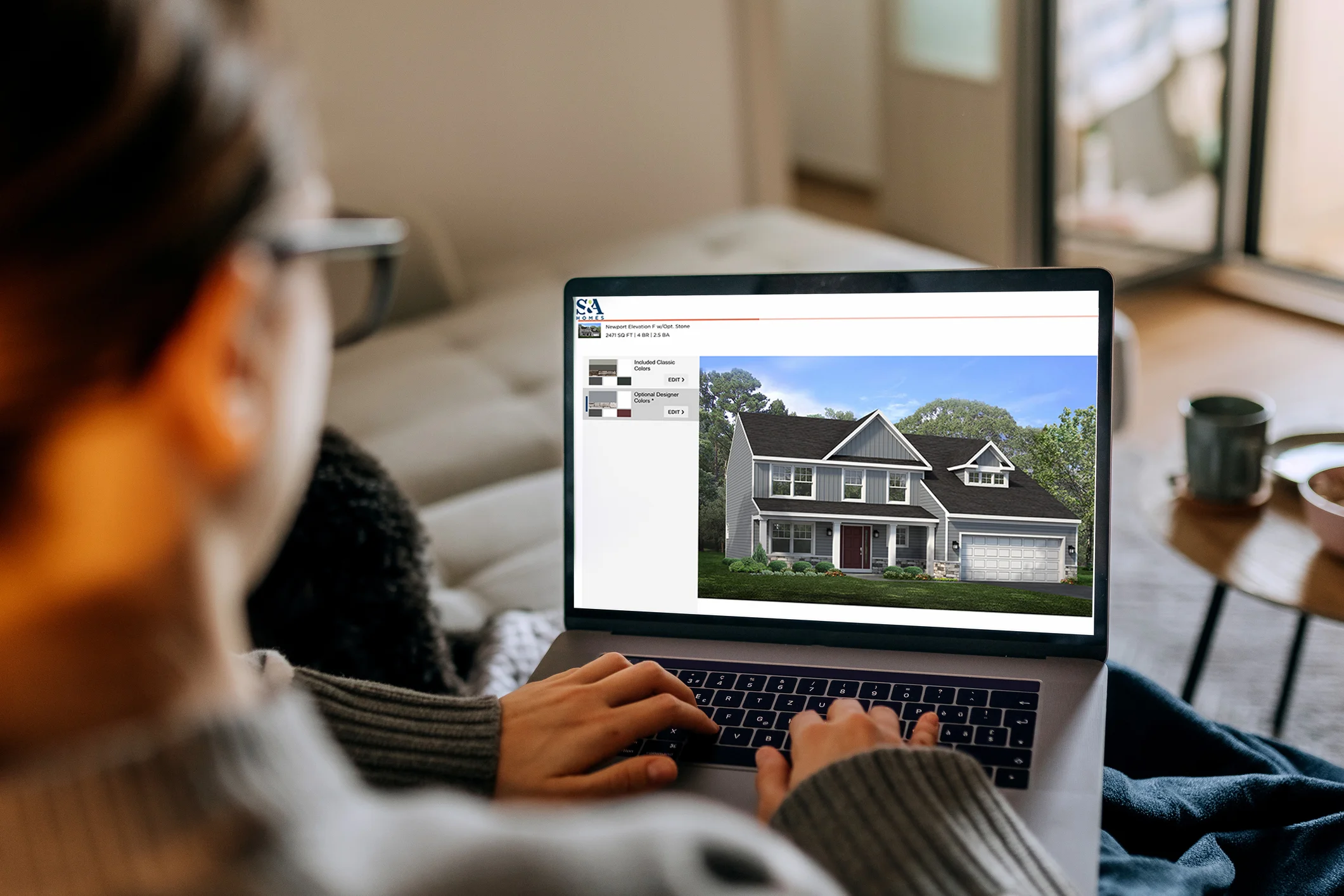 Person using a laptop to visualize S&A Homes exterior elevations, showing a two-story home design on screen