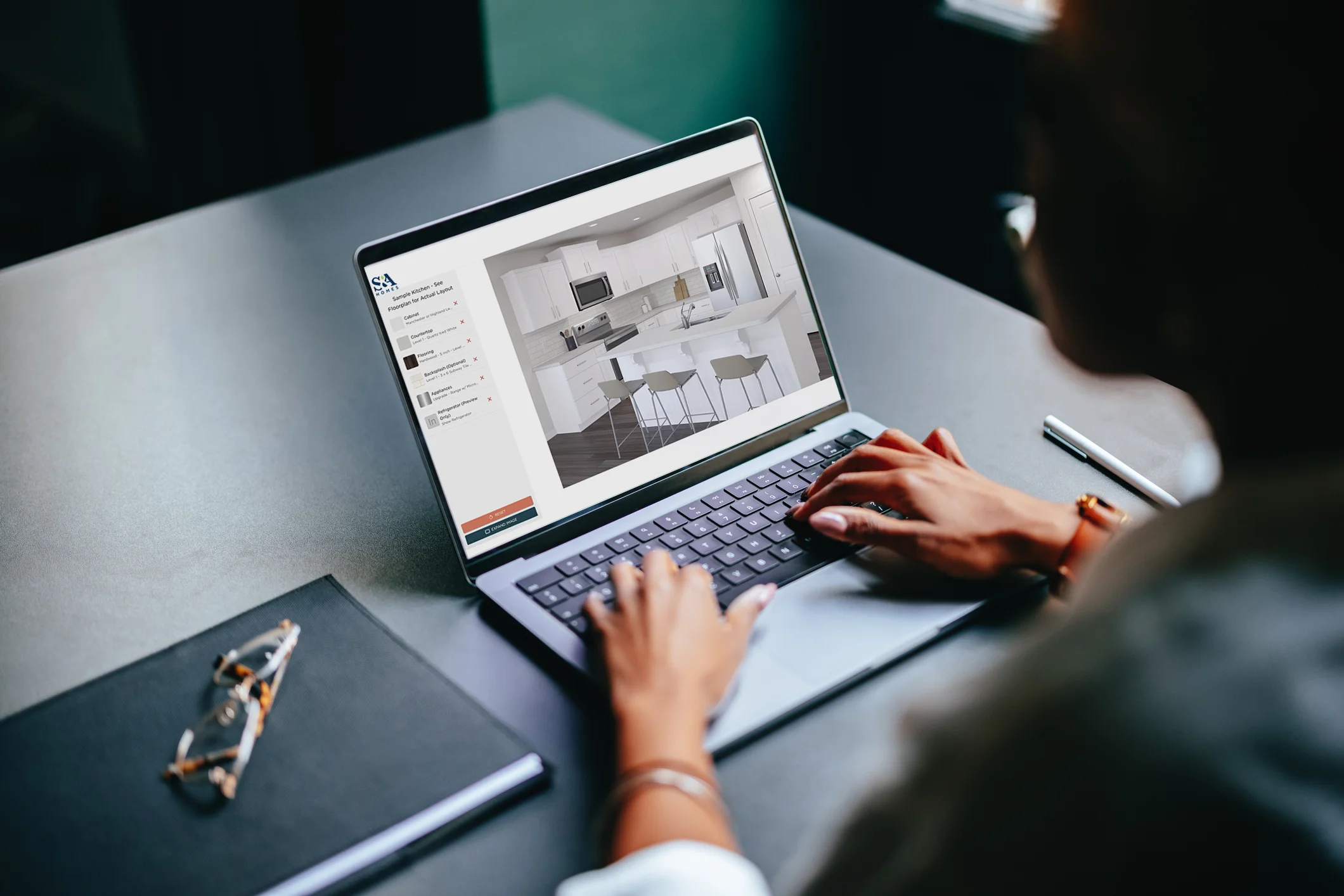 Person working on a laptop displaying an S&A Homes kitchen design tool, previewing cabinetry, island seating, and layout options