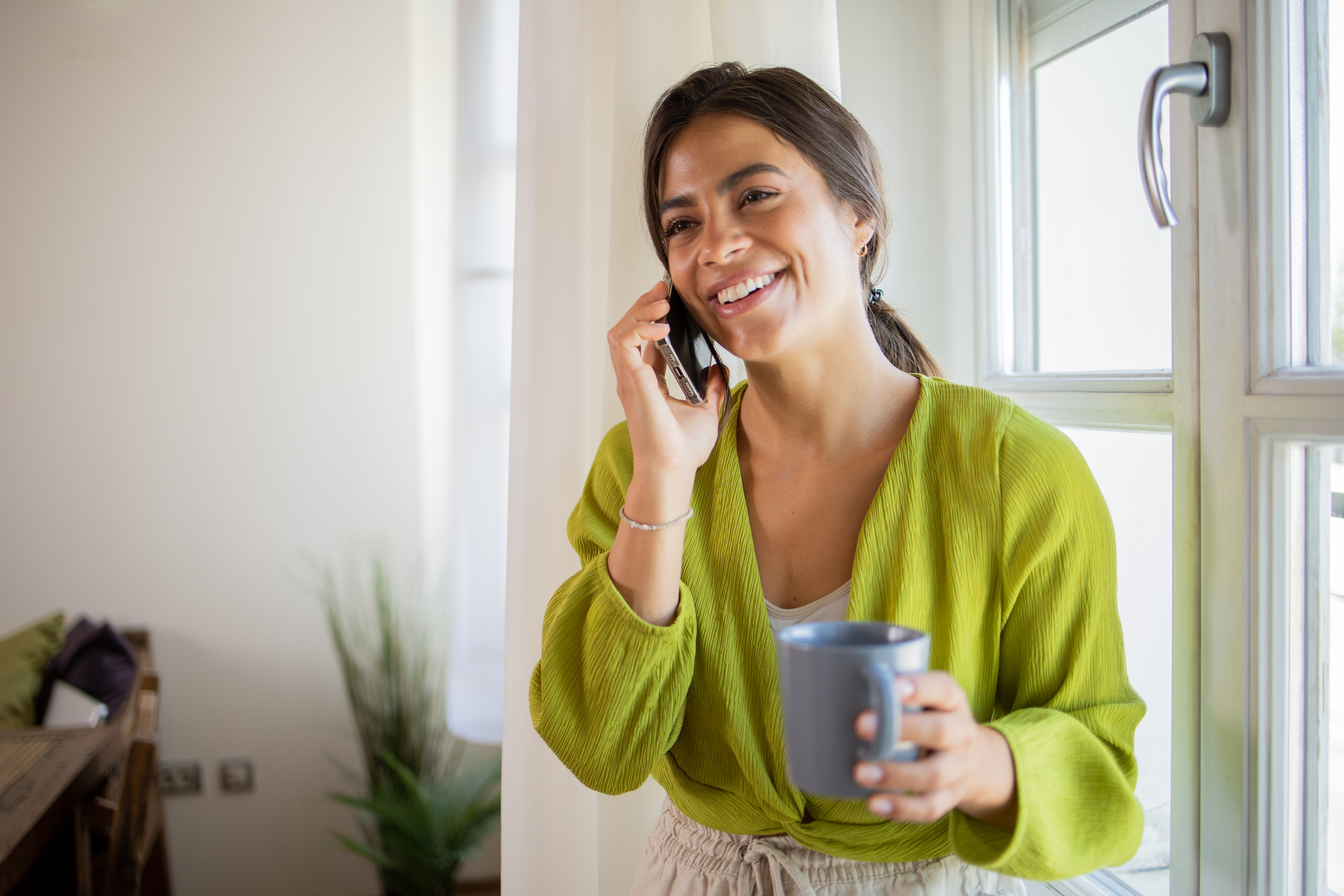 Woman with a cup of coffee in her home speaking with a customer care coordinator on the phone.