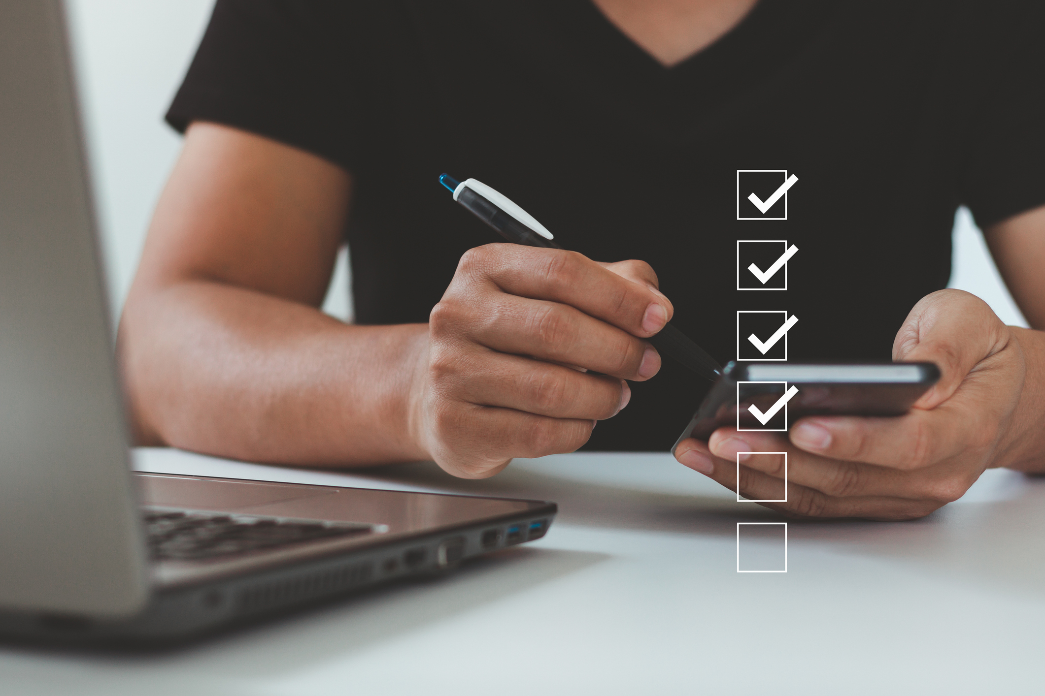 Individual sitting at a table with a pen, notebook and laptop. A checklist overlays the photo signifying a checklist is being reviewed.