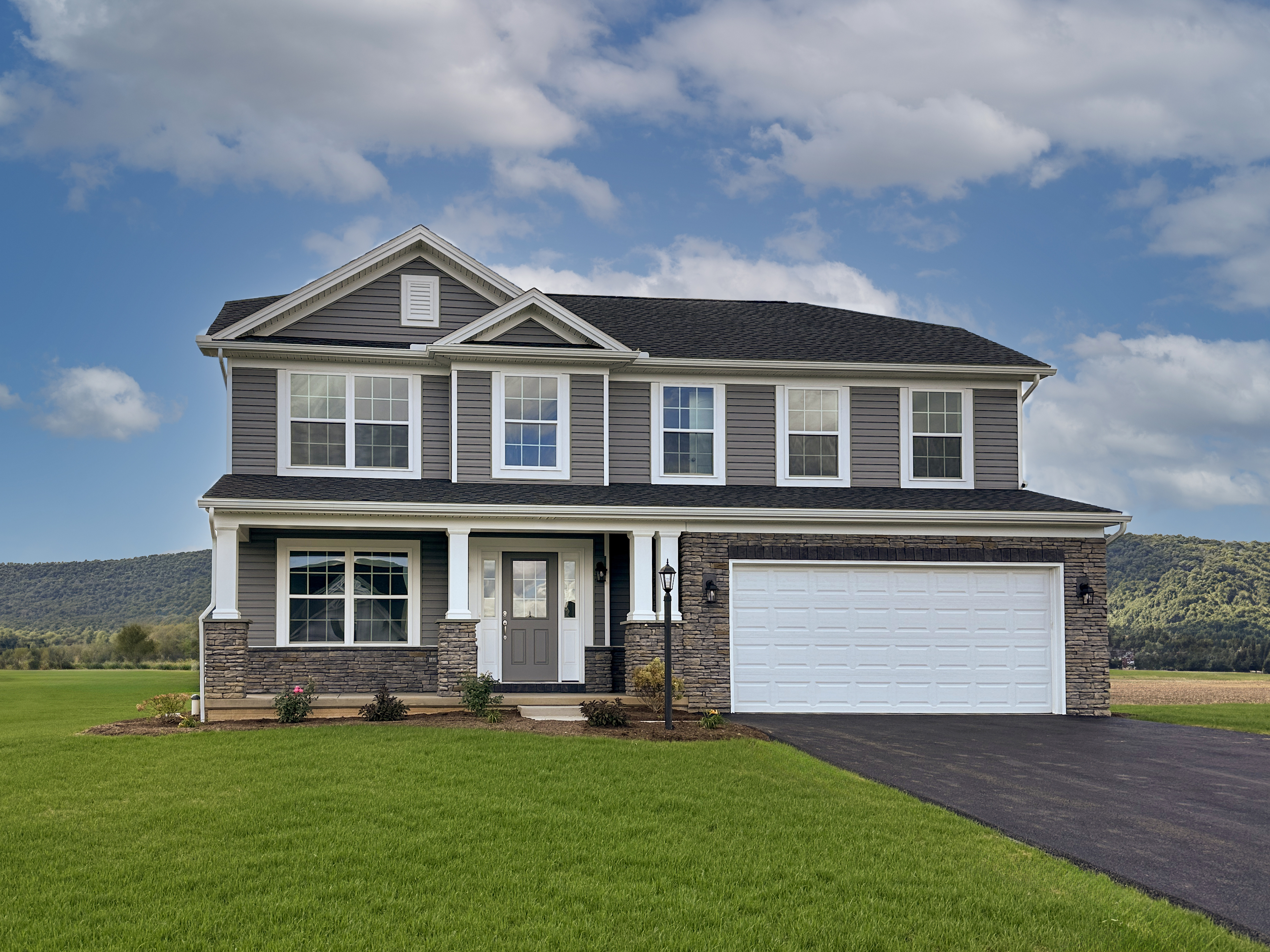 Exterior front view of a brand new 2-story home with a 2-car garage and front porch on a cloudy summer day.